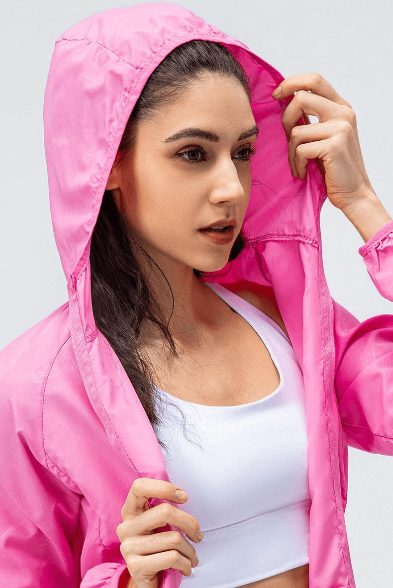 Woman wearing a pink waterproof windbreaker jacket with hood, designed for running and outdoor sports.